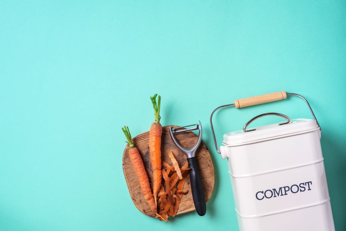 Top view of kitchen food waste collected in a compost bin with peeled vegetables on a chopping board