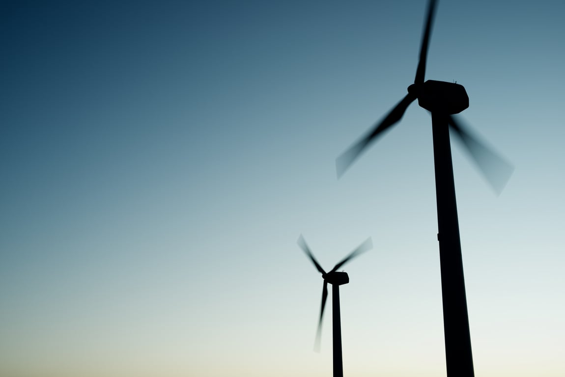 Silhouette of wind turbines against a pale blue sky, representing renewable wind energy