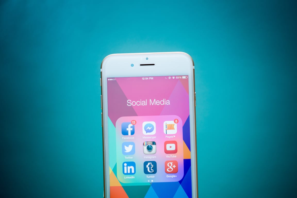 Smartphone screen displaying various social media app icons including Facebook, Twitter, Instagram, LinkedIn and more on a colorful geometric background