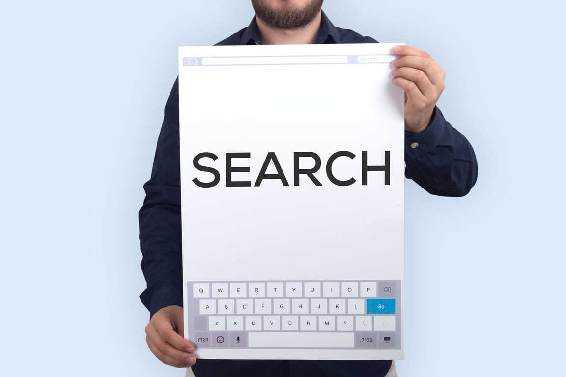 Close-up of hands holding printout of browser search bar with "SEARCH" above it