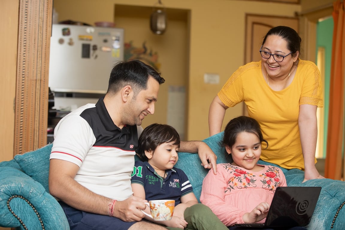 A family of four, parents and kids, looking at a laptop and smiling.
