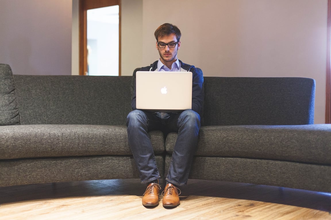 A man working seriously on a laptop while sitting on a couch.
