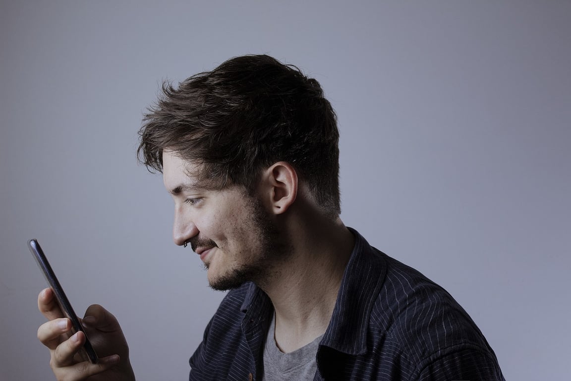 A man smiling while looking at his phone.