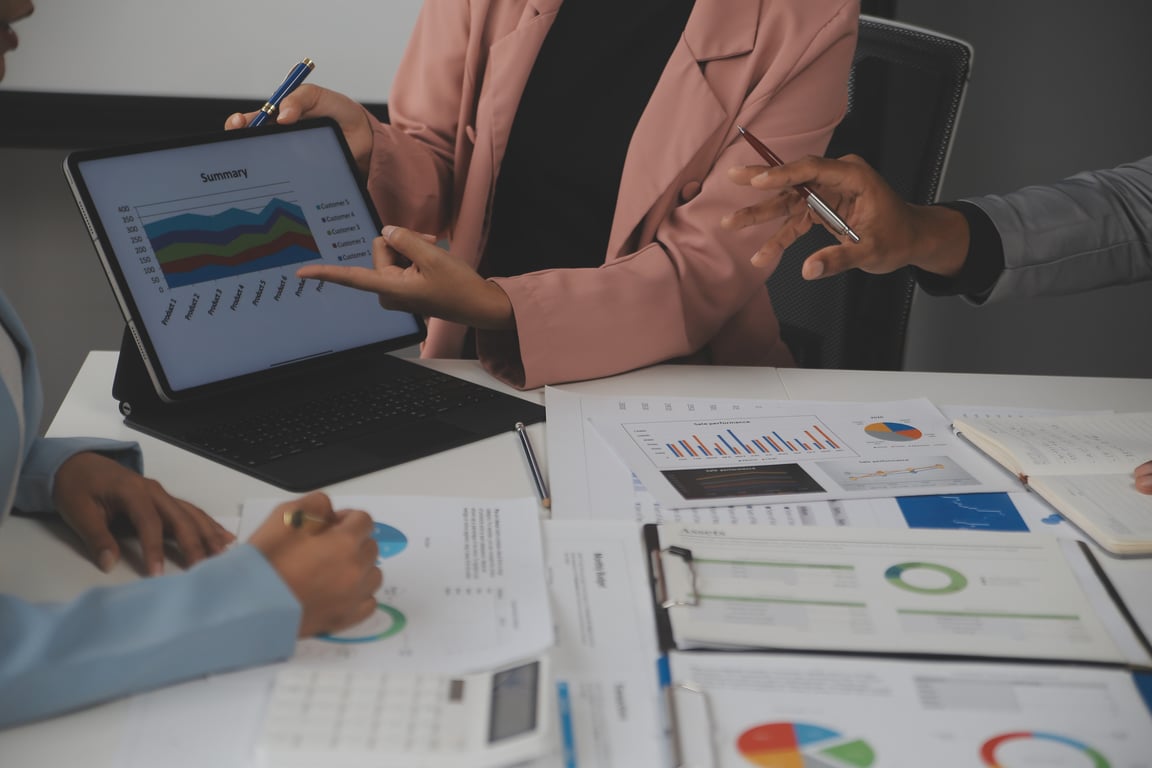 Business professionals analyzing revenue management data on tablet and printed reports with charts and graphs during strategic planning meeting