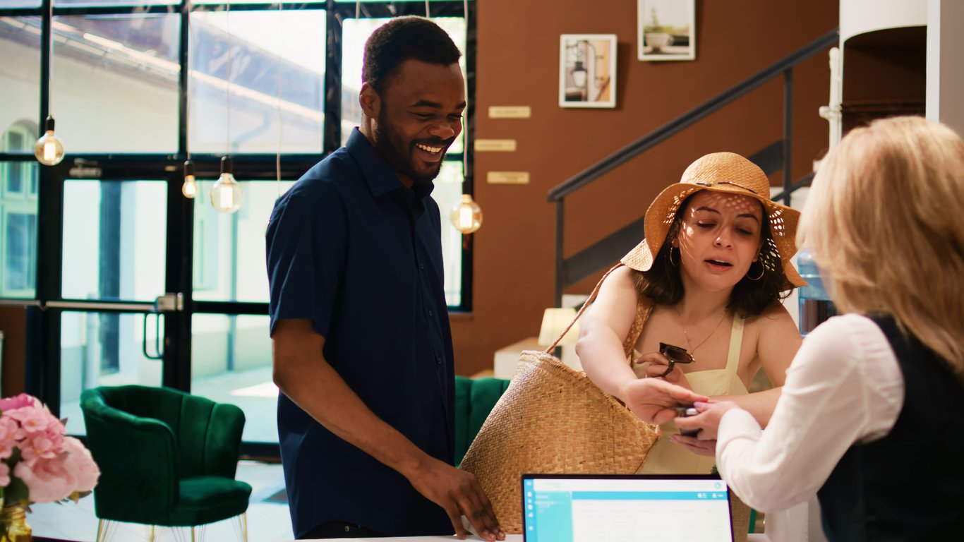 A professional photo of happy hotel staff interacting with customers at a modern reception desk, demonstrating the benefits of expert hotel system integration services and automation.