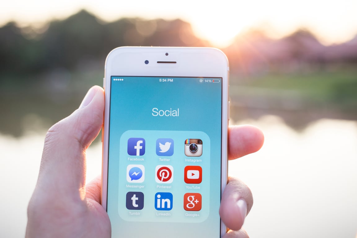 Hand holding smartphone showing various social media app icons