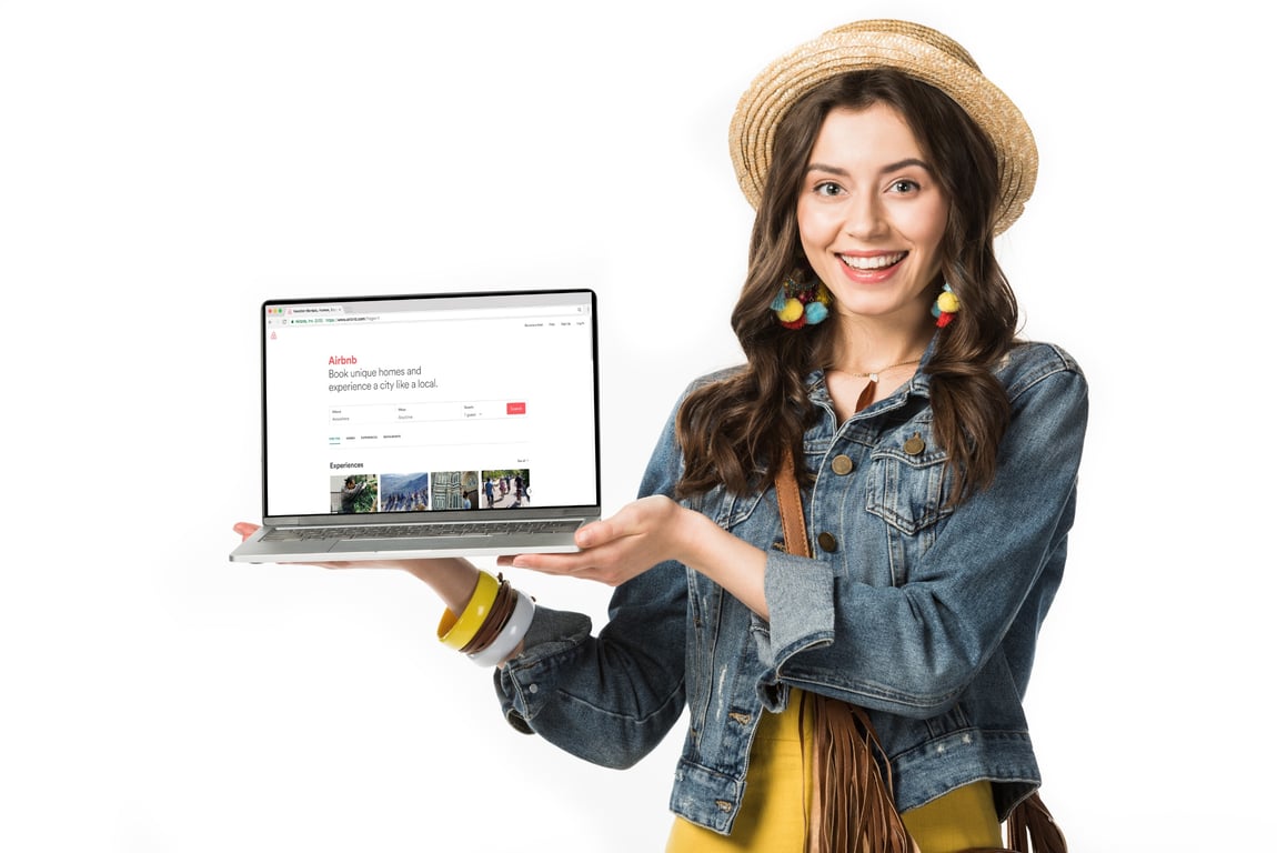 Smiling woman holding a laptop displaying Airbnb, one of the recommended OTAs for property rentals.