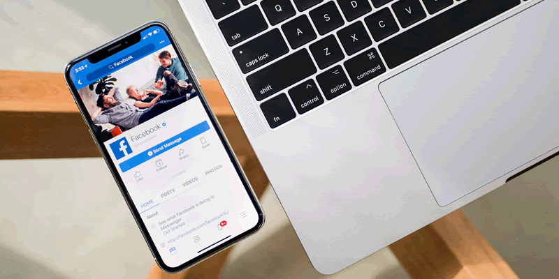 Smartphone displaying Facebook app alongside laptop on desk