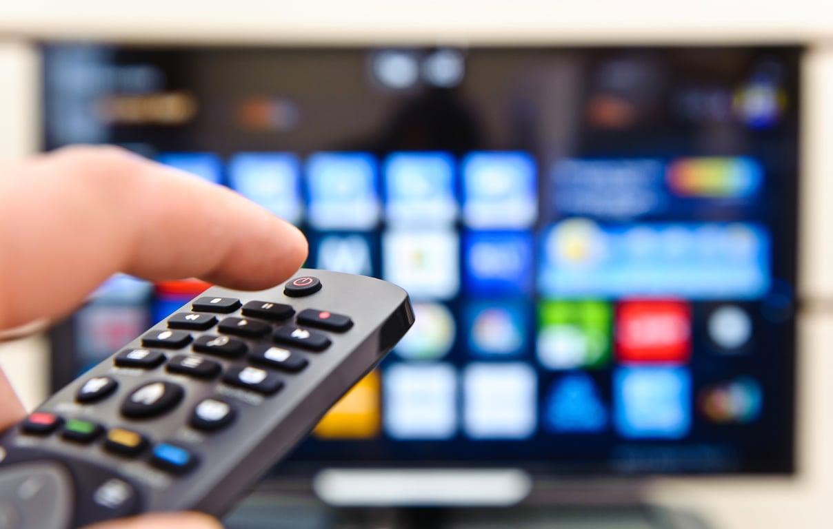 A hand holding a remote control aimed at a smart TV displaying streaming options