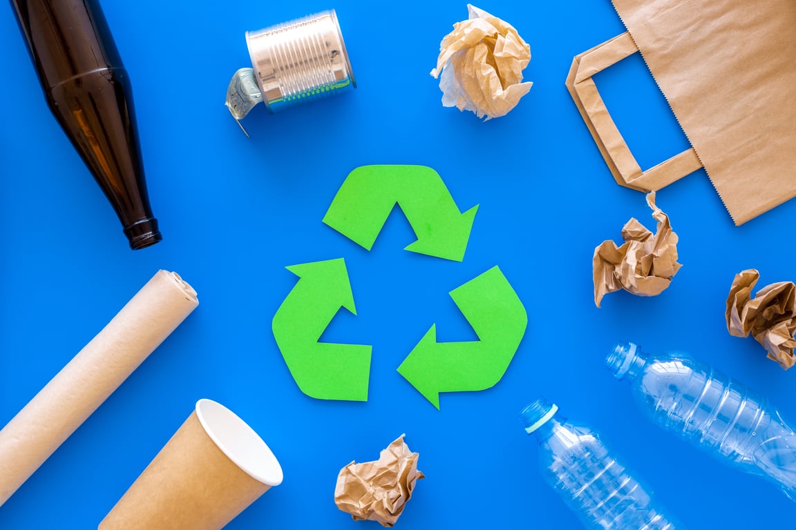 Green recycle symbol surrounded by plastic waste items like bottles, cups and packaging on blue background