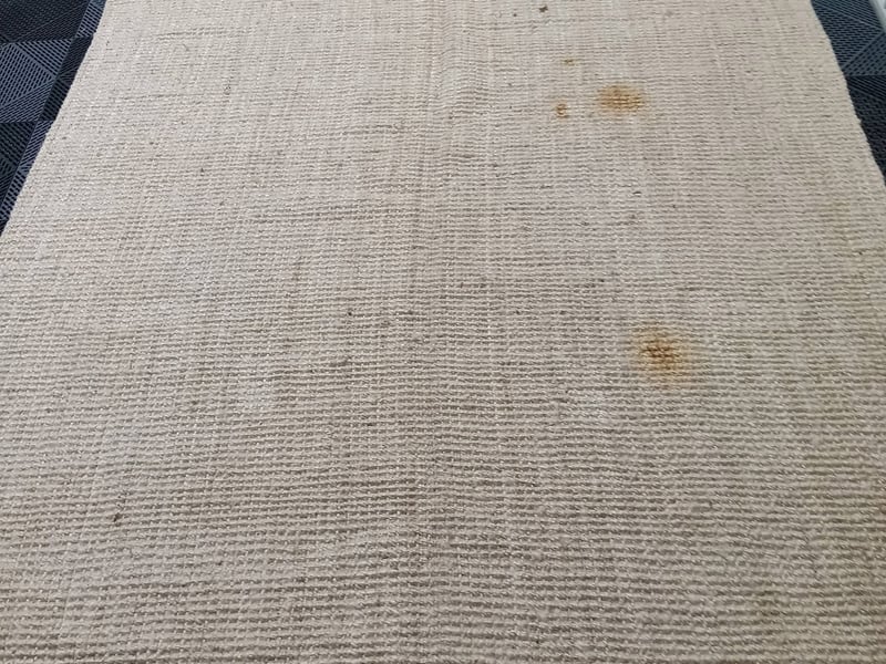 A beige natural-fiber area rug with a set-in brown stain before cleaning