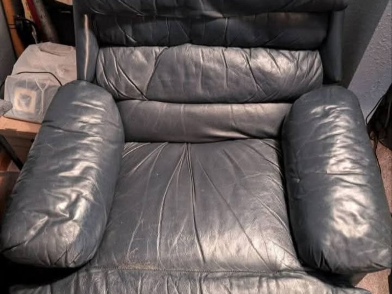 A blue leather recliner looking dull and worn with soiled creased cushions before cleaning