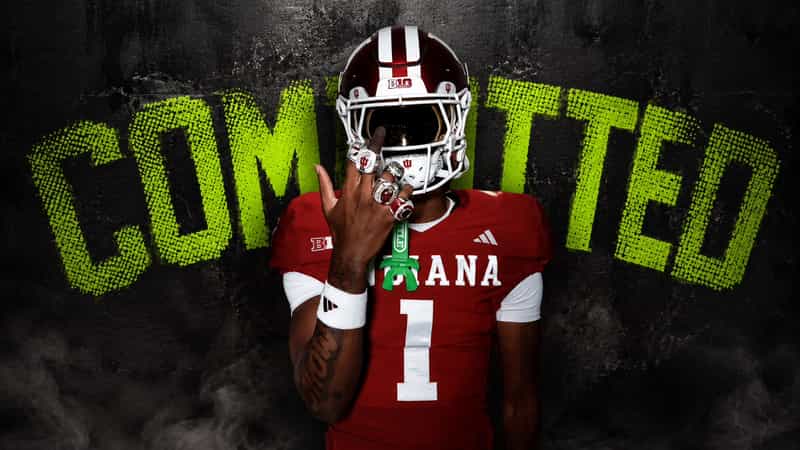 Monshun Sales in a red Indiana Hoosiers number 1 uniform and helmet in front of a graphic that reads COMMITTED.