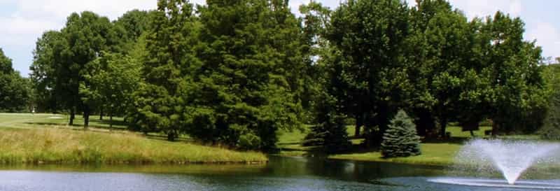 Golf course pond with a fountain and trees at Greensburg Country Club in Greensburg