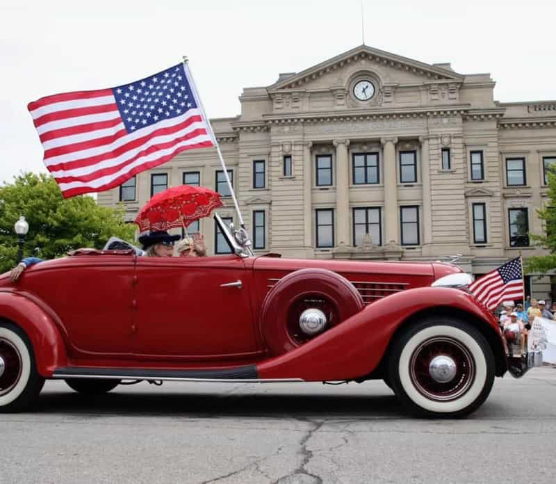 Red vintage Auburn convertible with American flags passes the DeKalb County Courthouse during the Parade of Classics in Auburn, Indiana