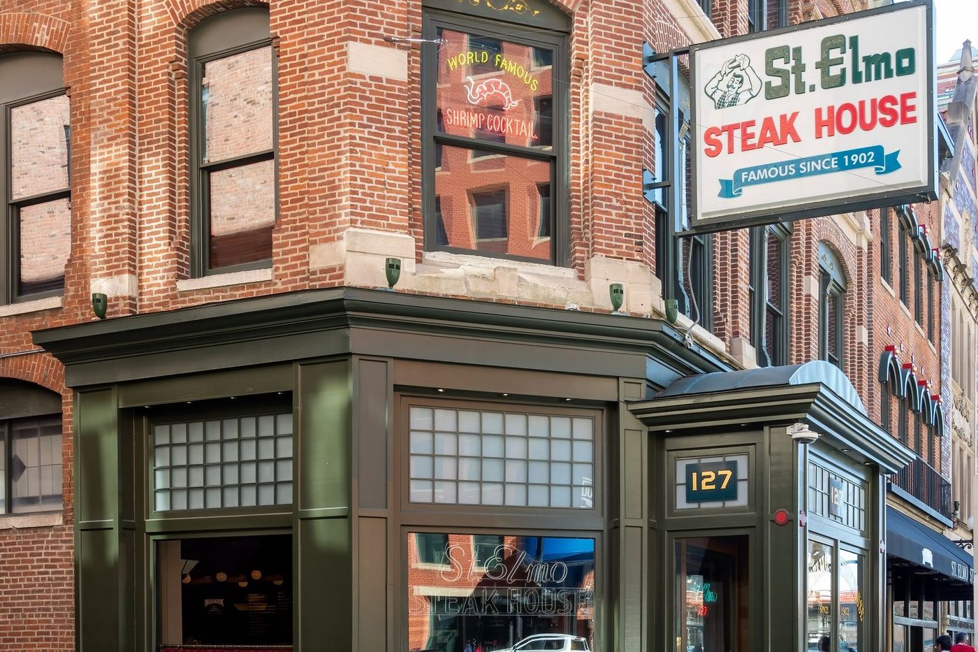 The green storefront and corner entrance of St. Elmo Steak House in downtown Indianapolis, with its Famous Since 1902 sign and a World Famous Shrimp Cocktail window above the door at 127