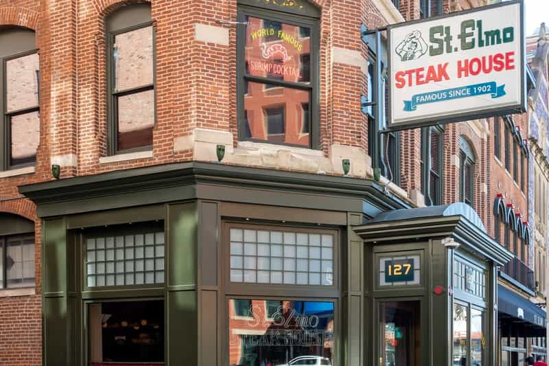 The green storefront and corner entrance of St. Elmo Steak House in downtown Indianapolis, with its Famous Since 1902 sign and a World Famous Shrimp Cocktail window above the door at 127