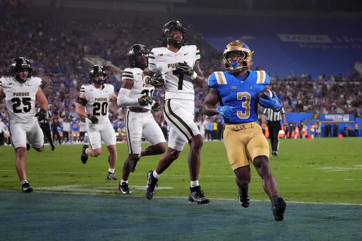 UCLA running back in a blue No. 3 jersey carries the ball toward the end zone as Purdue defenders chase him at the Rose Bowl