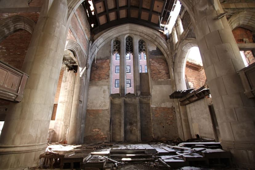 Gothic stone columns and arched windows inside the ruined City Methodist Church sanctuary in Gary, Indiana, with collapsed roof beams and debris on the floor