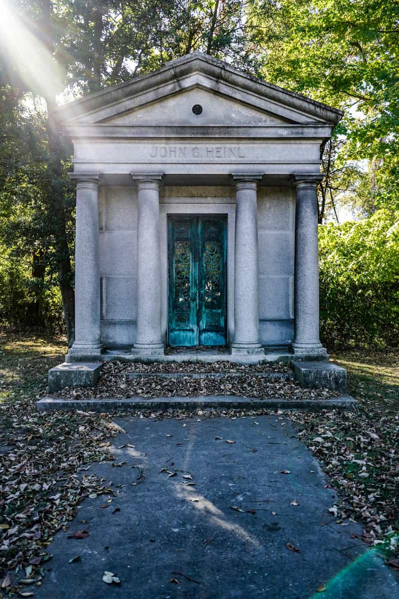 The John G. Heinl mausoleum at Highland Lawn Cemetery in Terre Haute, a granite temple-front tomb with four columns and teal double doors among fallen leaves