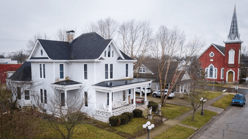 White two-story Whispers Estate house in Mitchell next to a red brick church