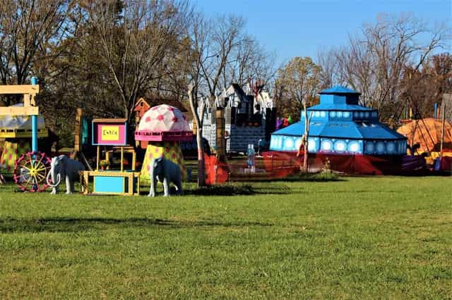 Colorful themed attractions at The Fun Farm in Fort Wayne, including a blue alien spaceship, a castle, a giant mushroom and elephant sculptures across a grassy field.