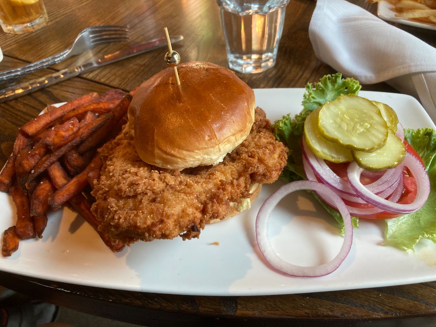 A breaded pork tenderloin sandwich on a brioche bun with sweet potato fries, pickles, and red onion at a Hamilton County restaurant.