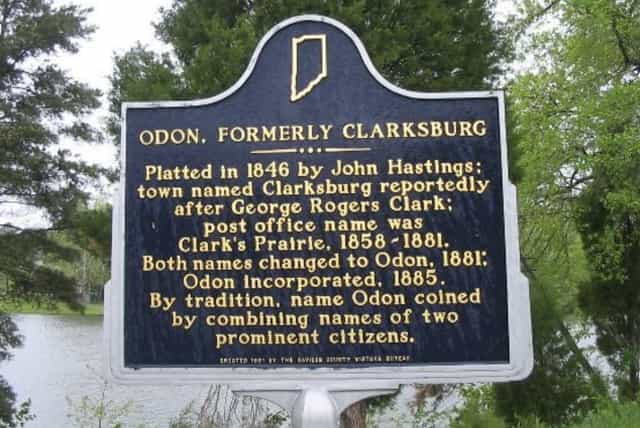 Blue-and-gold Indiana historical marker titled Odon, Formerly Clarksburg beside a pond, noting the town was platted in 1846 and renamed Odon in 1881.