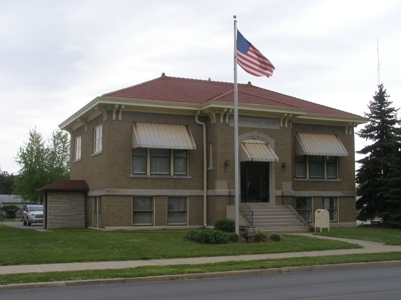Brick Carnegie Public Library building with a red tile roof, striped awnings and an American flag out front in Royal Center, Indiana