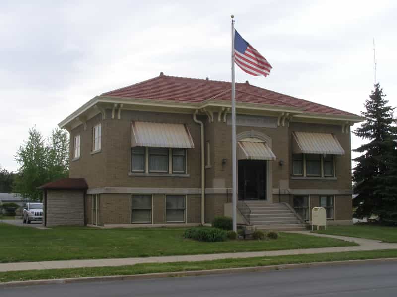 Brick Carnegie Public Library building with a red tile roof, striped awnings and an American flag out front in Royal Center, Indiana