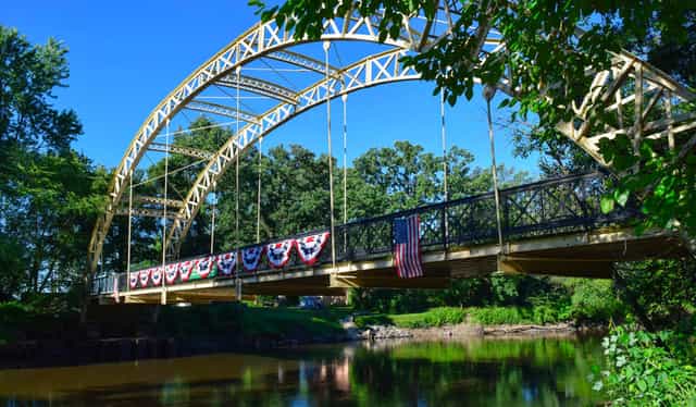 Dunn’s Bridge, a yellow steel arch bridge hung with patriotic bunting and an American flag, spanning the Kankakee River near Wheatfield, Indiana.
