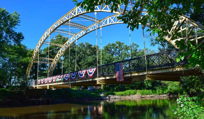 Dunn’s Bridge, a yellow steel arch bridge hung with patriotic bunting and an American flag, spanning the Kankakee River near Wheatfield, Indiana.