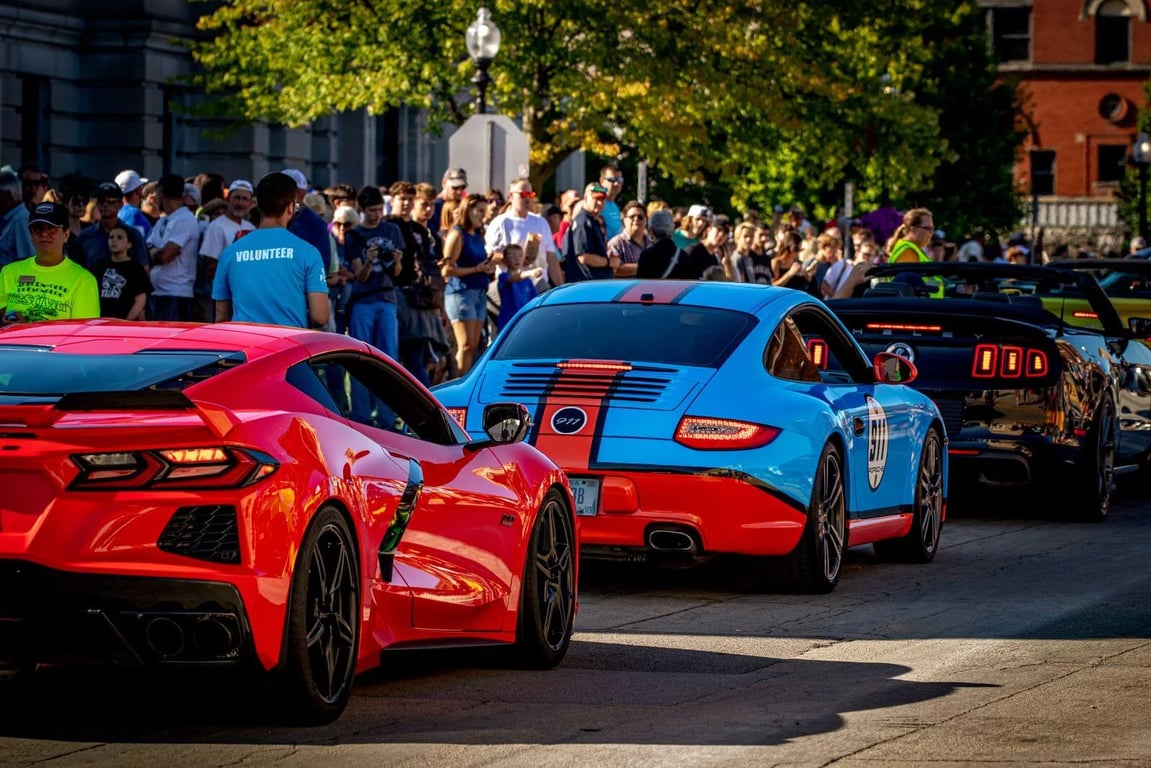 Red Corvette, blue Porsche, and black Mustang cruise past spectators during Fast and Fabulous in downtown Auburn