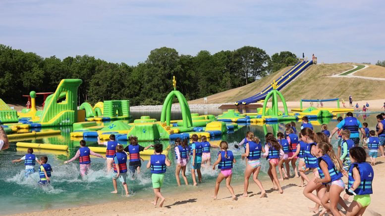 Children in life jackets running into the water toward inflatable obstacles at SKYLAKE Adventures in Sheridan, Indiana