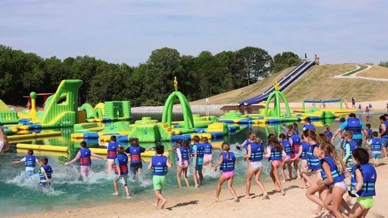 Children in life jackets running into the water toward inflatable obstacles at SKYLAKE Adventures in Sheridan, Indiana