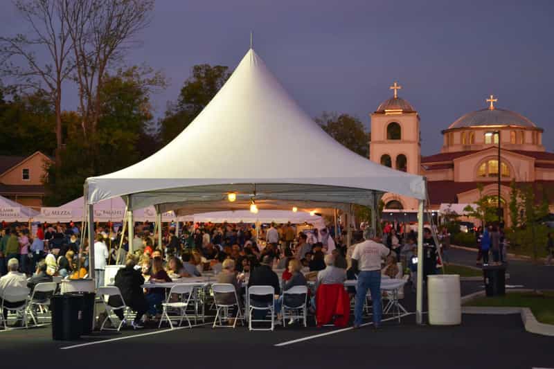 The dining tent full of guests at dusk beside St. George church during the Middle Eastern Festival