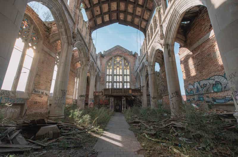 Interior of the roofless City Methodist Church in Gary, Indiana, with Gothic stone arches, a stained-glass window at the far end, and weeds and debris covering the floor