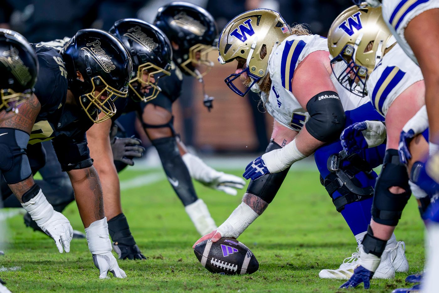 Purdue defensive linemen in black helmets line up across from Washington's center as he grips the ball before the snap at Ross-Ade Stadium
