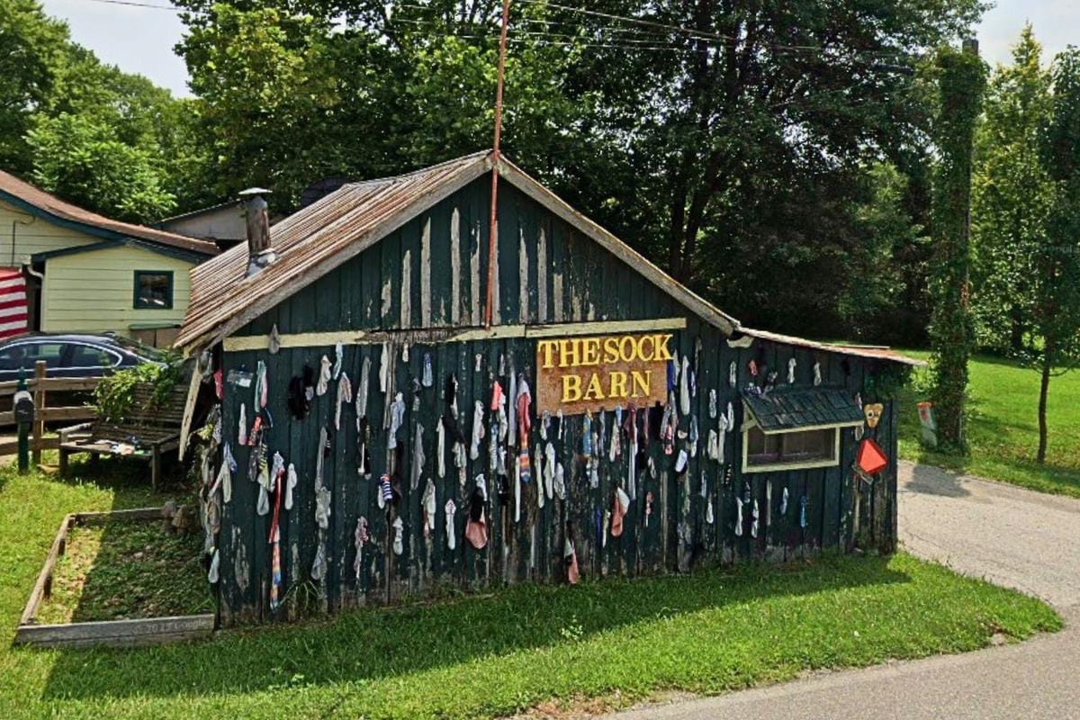 The Sock Barn outside Nashville, Indiana, a dark green wooden barn with a hand-painted sign, its side wall covered in dozens of hanging socks