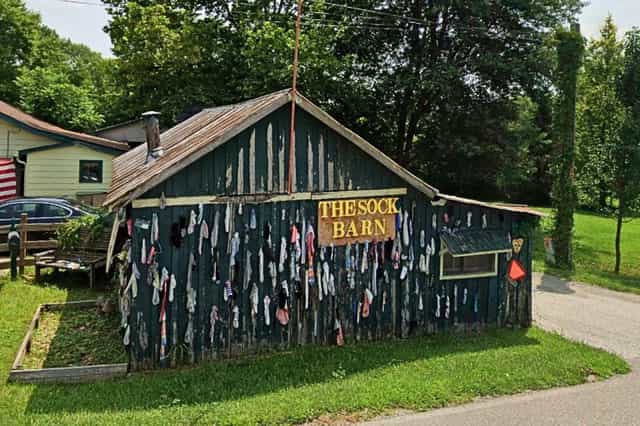 The Sock Barn outside Nashville, Indiana, a dark green wooden barn with a hand-painted sign, its side wall covered in dozens of hanging socks