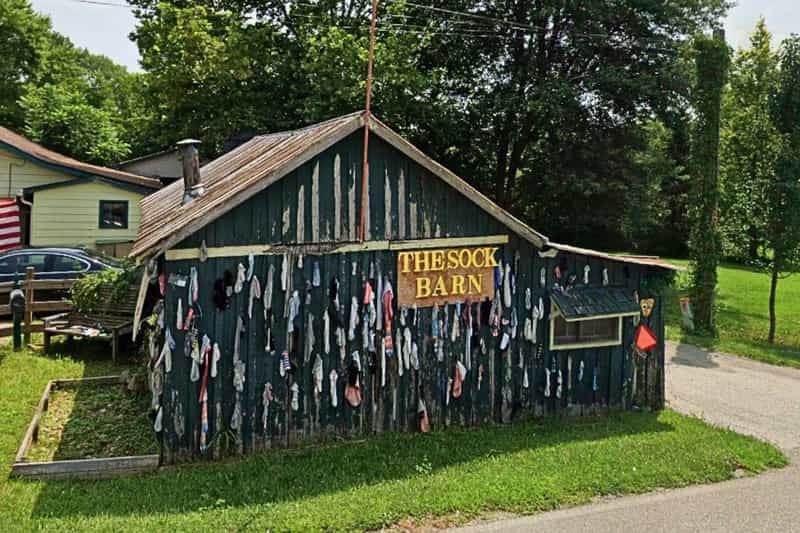 The Sock Barn outside Nashville, Indiana, a dark green wooden barn with a hand-painted sign, its side wall covered in dozens of hanging socks