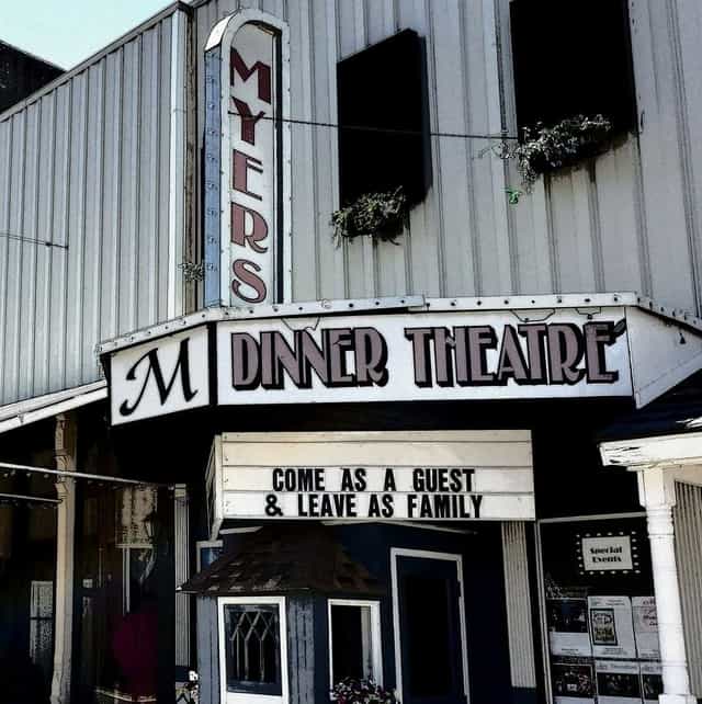 The vertical Myers marquee and Dinner Theatre sign on the front of The Harmony Theater in downtown Hillsboro, Indiana, with a message board reading Come as a Guest and Leave as Family