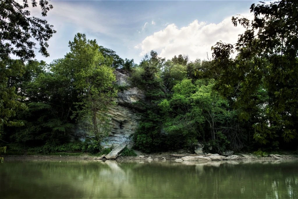 A limestone bluff draped in green trees reflected in the calm, jade-colored Wabash River near Lagro, Indiana