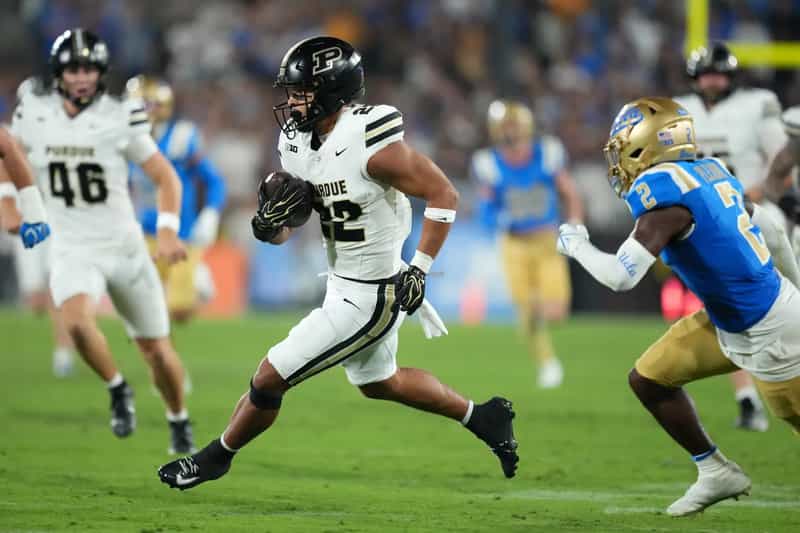 Purdue ball carrier in a white No. 22 jersey runs upfield past a UCLA defender at the Rose Bowl