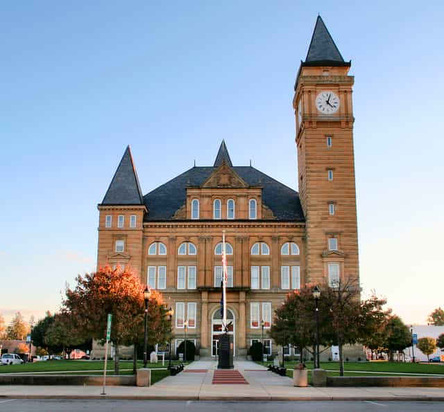 The Tipton County Courthouse in Tipton, Indiana, a sandstone building with steep slate roofs and a tall clock tower, seen from the street on a fall evening