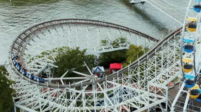 Aerial view of a wooden roller coaster curving out over Lake Shafer at Indiana Beach in Monticello, Indiana, with a Ferris wheel beside the boardwalk.