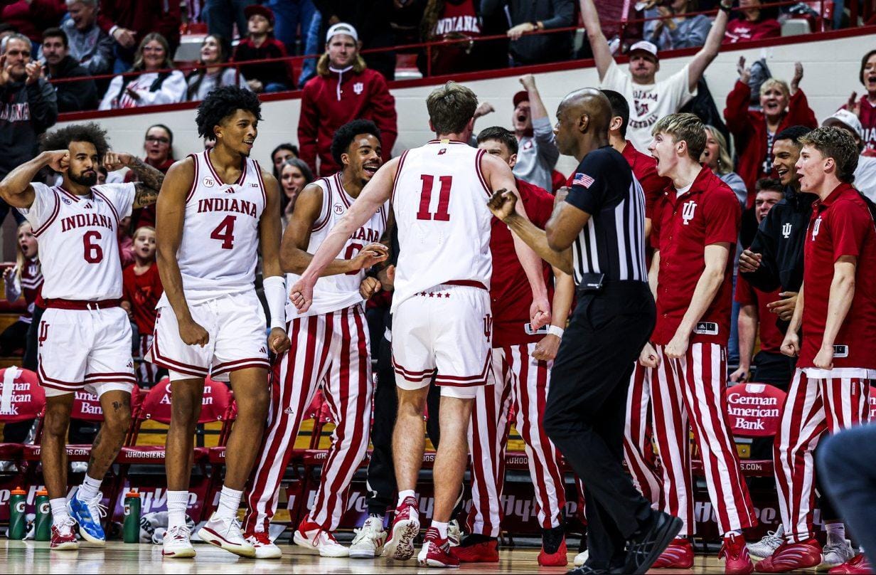 Indiana Hoosiers men's basketball players in candy-stripe uniforms celebrate on the court at Assembly Hall as teammates rush in from the bench.