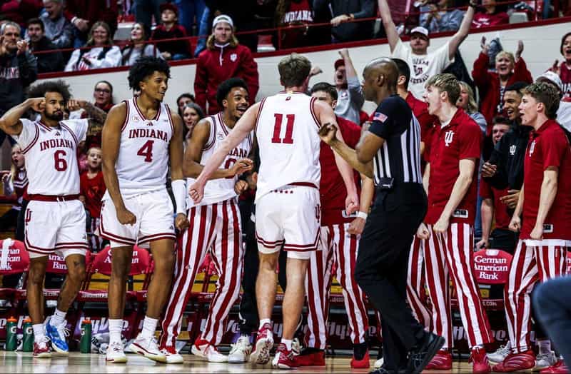 Indiana Hoosiers men's basketball players in candy-stripe uniforms celebrate on the court at Assembly Hall as teammates rush in from the bench.