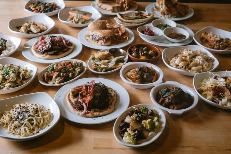 A long wooden table covered with dozens of Mediterranean dishes at Corridor in Indianapolis, including flatbreads topped with pickled onions and herbs, fresh pasta, olives, salads, sandwiches and roasted vegetables