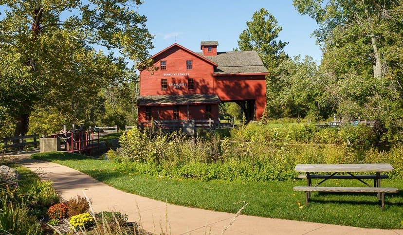 Red Bonneyville Mill, established 1832, beside a paved walking path and picnic table at Bonneyville Mill County Park near Bristol, Indiana